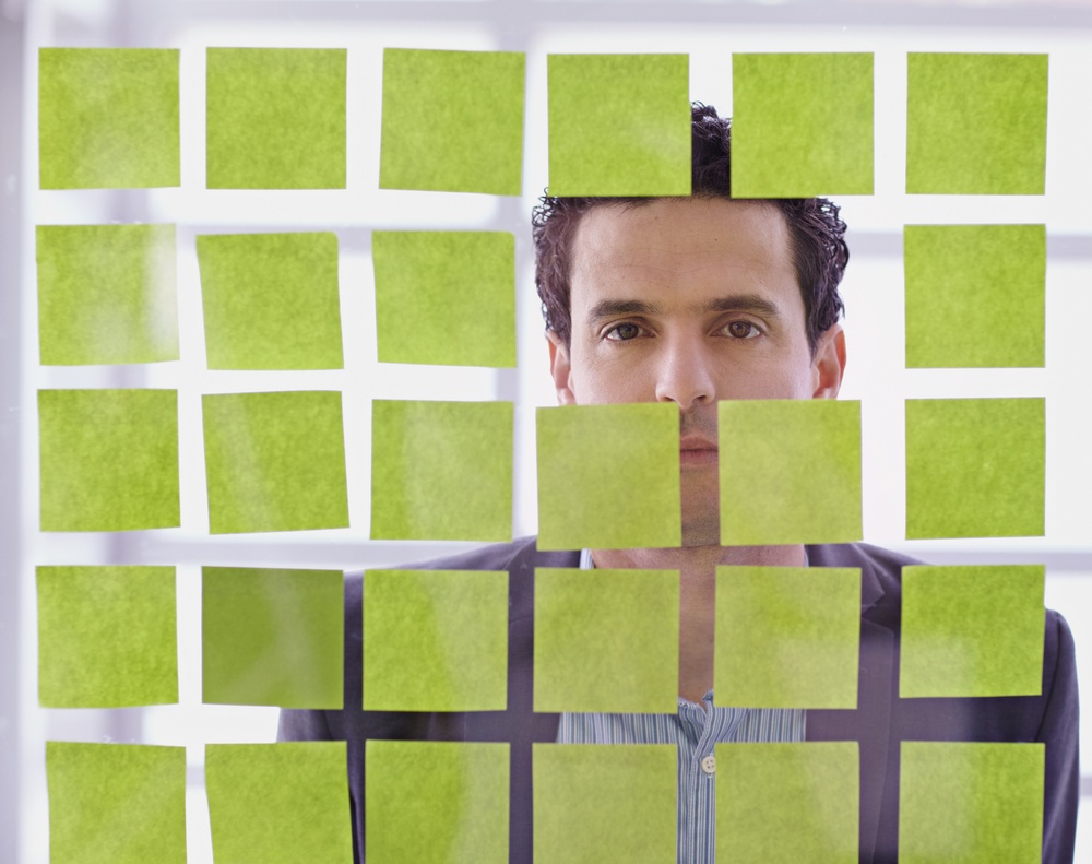 Portrait of a middle eastern business man behind sticky notes in bright glass office